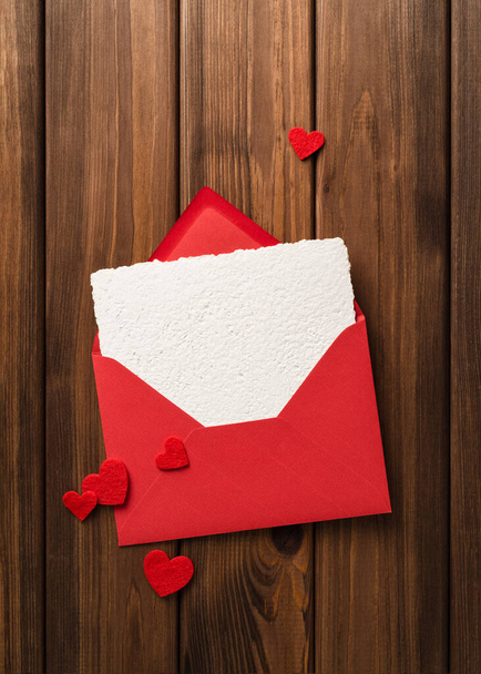 バレンタインデーの背景には、ヴィンテージの木のテーブルと赤いハートの封筒にグリーティングカードテンプレートがあります - 写真・画像