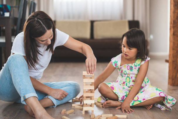 Молодая мать со своей маленькой дочерью играют в игру в деревянном блоке - Фото, изображение