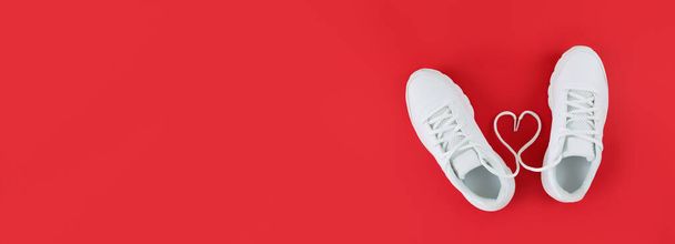 Witte sportschoenen en hartvorm van veters op een rode achtergrond. Eenvoudige platte lay met kopieerruimte. - Foto, afbeelding
