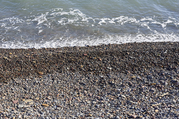 Kleine rotsen strand kust, unfocused achtergrond, niemand, voorgrond, zonnige, grote en kleine stenen - Foto, afbeelding