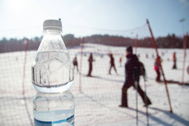 Arka planda bir şişe su, Polonya 'da kayak parkı. Yeni yıl. İnsanlar kayağa gider, asansöre giderler. - Fotoğraf, Görsel