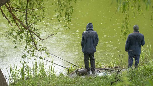 Un pêcheur pêche dans le lac sur une canne à pêche sous la pluie. - Photo, image