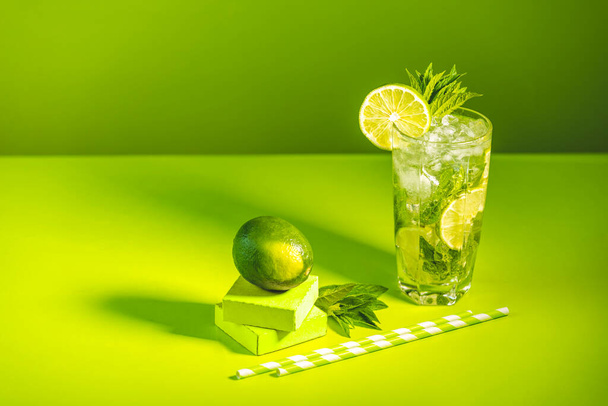 Творческий подход к напиткам. Свежий коктейль Мохито с лаймом и мятой в бокале хайбол с капельками воды на зеленом фоне в ярком свете, освежающие напитки Мохито. Летние каникулы и вечеринка - Фото, изображение