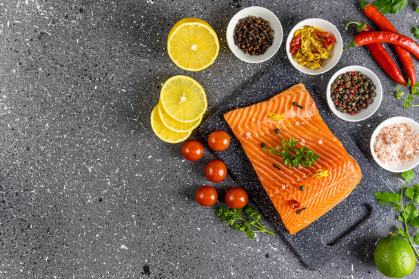 Raw salmon fillet and ingredients for cooking, seasonings and herbs on a dark background. Top view - Photo, Image