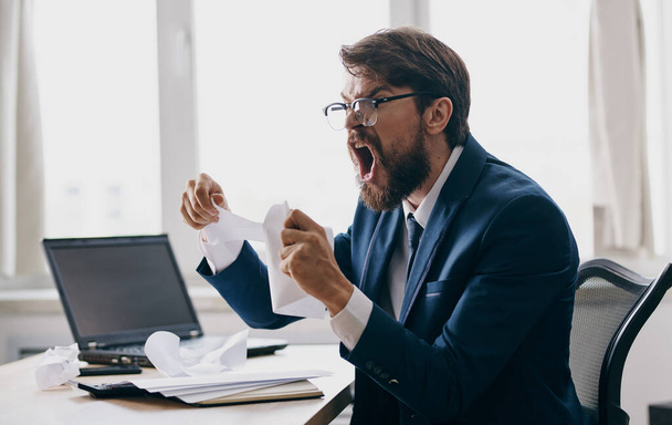 Impulsieve man met witte vellen papier in handen emoties kantoor business finance laptop - Foto, afbeelding