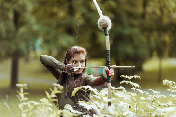 Warrior medieval woman with bow hunting in green forest, close-up - Fotó, kép