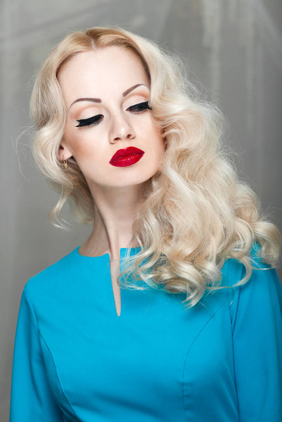 Belle jeune femme blonde aux cheveux bouclés et maquillage, en robe bleue. - Photo, image