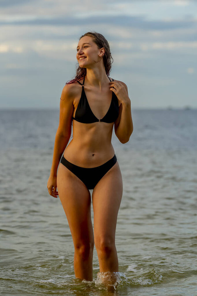 A beautiful Brunette bikini model enjoys the weather outdoors on the beach - Photo, Image