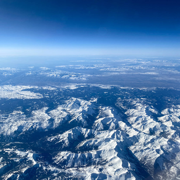 山、雪、雲と明るい青空の飛行機の窓からの空の景色. - 写真・画像