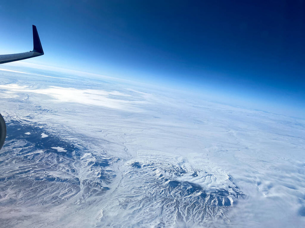 Una vista aérea desde una ventana de avión de montañas, nieve, nubes y cielos azules brillantes. - Foto, Imagen