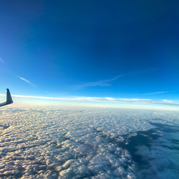 Eine Luftaufnahme aus einem Flugzeugfenster aus Wolken mit strahlend blauem Himmel. - Foto, Bild
