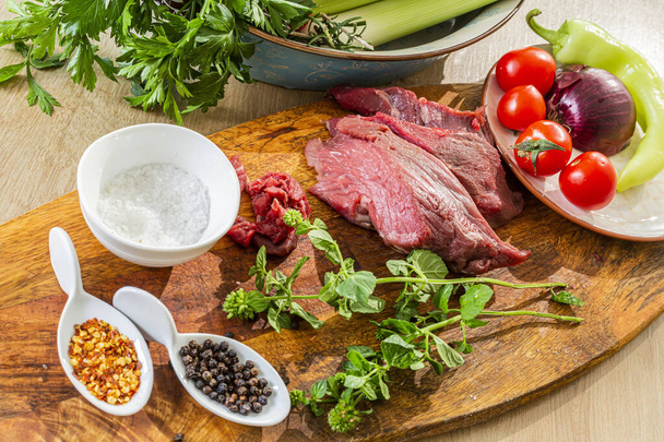 Közelkép a nyers húsról egy előkészületre kész konyhai falemezen. Láthatjuk a különböző zöldségek körül, mint egy oldalsó étel és kis konyhai tálak fűszerekkel. - Fotó, kép