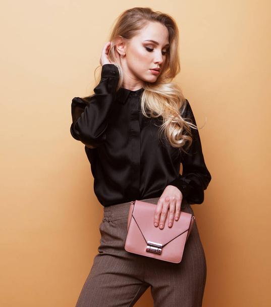Young beautiful blond woman in a brown blouse and pants holds a pink handbag and posing on a beige background.Fashion and people concept. - Photo, image