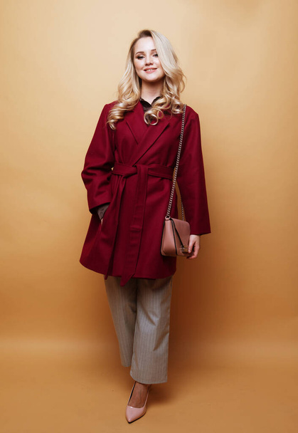 Beautiful young blond woman posing in nice clothes, red coat, handbag. Spring fashion concept. - Foto, Imagen