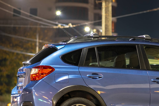 Niebieski samochód zaparkowany na jasno oświetlonej ulicy miejskiej w nocy. - Zdjęcie, obraz