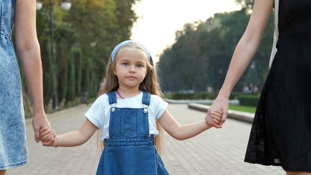 Nuori nainen ja hänen pieni tyttärensä pitkät hiukset kävelevät käsi kädessä kesäpuistossa. - Valokuva, kuva