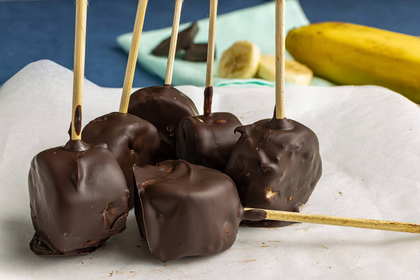 Stukken banaan op een stokje in chocolade glazuur op een bord. Close-up. - Foto, afbeelding