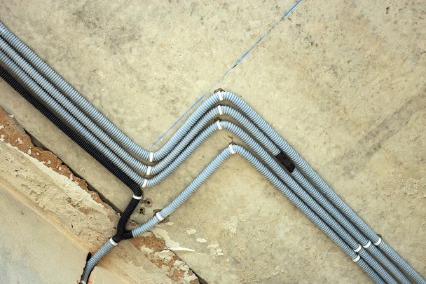 Электрические кабели, проложенные в защитном гофрировании, установленном на потолке и стене в строящемся помещении. - Фото, изображение