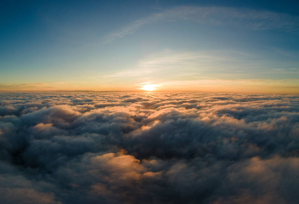Luchtfoto van felgele zonsondergang boven witte dichte wolken met blauwe lucht boven ons. - Foto, afbeelding