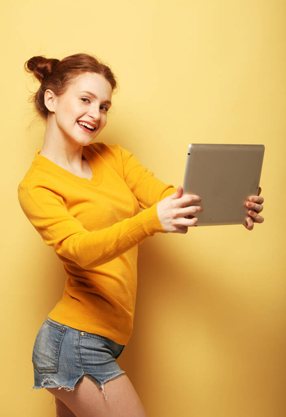 estilo de vida, tehnología y concepto de personas: Feliz pelirroja hembra tomando selfie con tableta digital sobre fondo amarillo - Foto, imagen