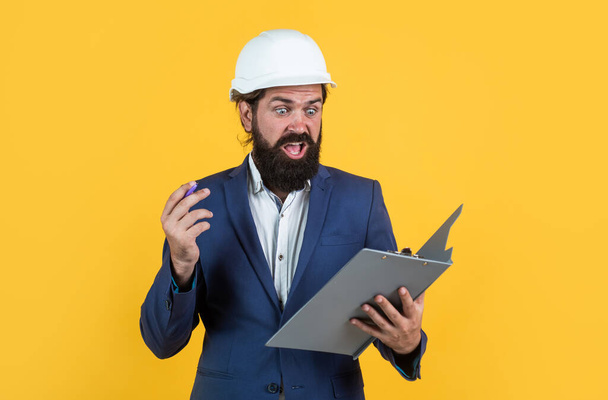 working on project. building concept. builder or engineer in hard hat. surprised mature architect in helmet making notes. brutal bearded man work on construction site with documents - Fotoğraf, Görsel