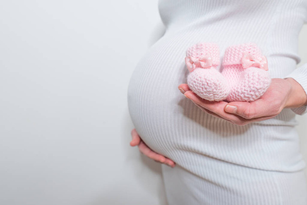 妊婦の腹の中の胎児のための小さな靴。妊娠中の女性はベッドルームで自宅でリラックスした小さな赤ちゃんの靴を保持。妊婦の腹の中の胎児のための小さな靴 - 写真・画像