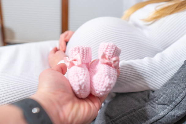 close-up van een schattige zwangere buik met baby schoenen, in de studio, op een witte achtergrond - Foto, afbeelding