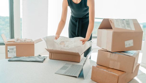 Selling clothing from home. Small business entrepreneur woman packing dress clothes in mailing box for shipping from online store - Foto, Bild