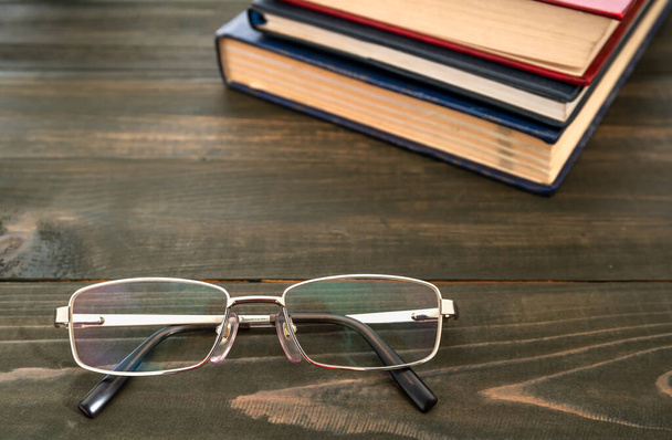 Szemüveg és egy halom keménykötésű könyv fából készült asztal fölött - Fotó, kép