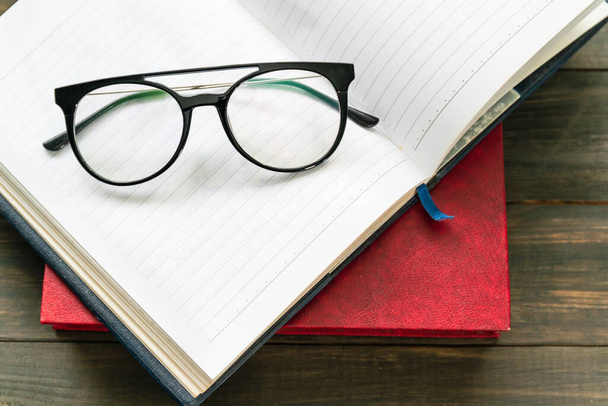 Reading glasses put on open book over wooden table - Fotó, kép