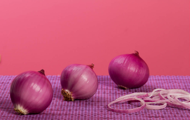 Oignons violets sur table violette et fond rose placés côte à côte et quelques tranches d'oignon côte à côte - Photo, image
