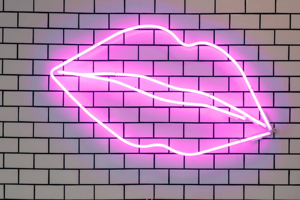 Lip shaped neon signs led glow decorative lights, wall decor. Purple fluorescent lamps on tiled white brick wall.  - Foto, Imagen