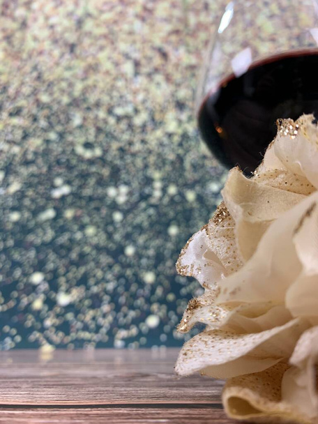 Δύο ποτήρια κόκκινο κρασί συνοδευόμενα από ένα λευκό τριαντάφυλλο σε ξύλινη βάση και φόντο με λάμψη, με χώρο για να τοποθετήσετε κείμενο - Φωτογραφία, εικόνα