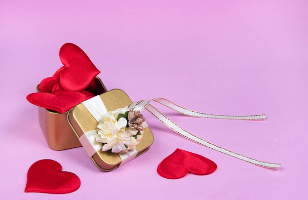 Golden gift box with flowers and ribbon. Red hearts inside gold box.  Decorations for Valentine day, holiday, wedding or birthday on pink background. Greeting card - Photo, image