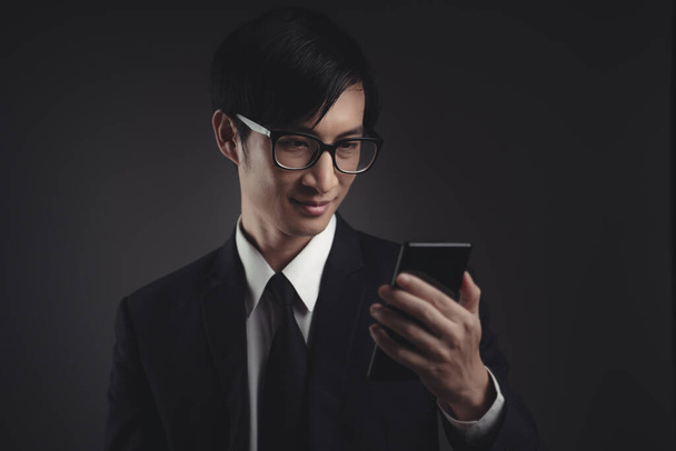 Азиатский бизнесмен в черном костюме счастлив и смотрит на смартфон. - Фото, изображение
