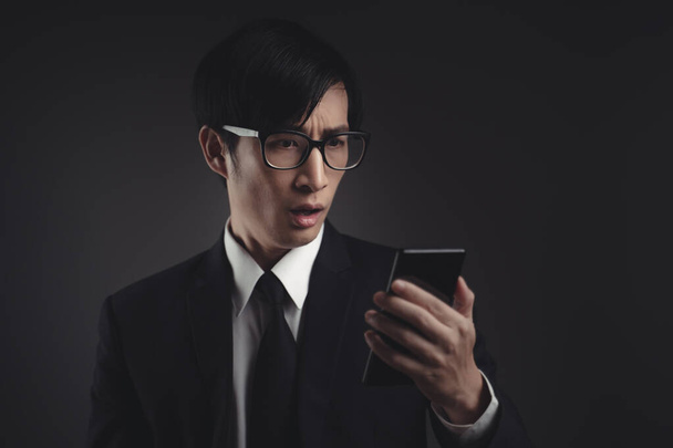 Азиатский бизнесмен в черном костюме беспокоится и смотрит на смартфон. - Фото, изображение