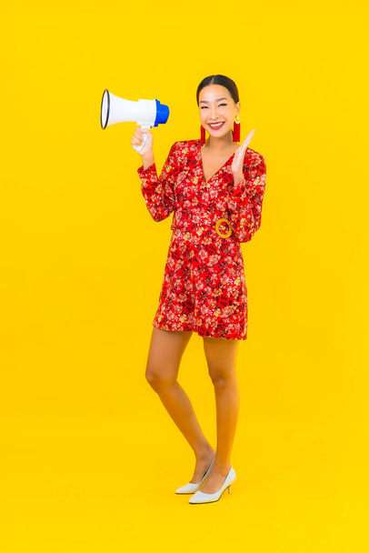 Portrét krásná mladá asijská žena s megafonem pro komunikaci na žlutém pozadí - Fotografie, Obrázek
