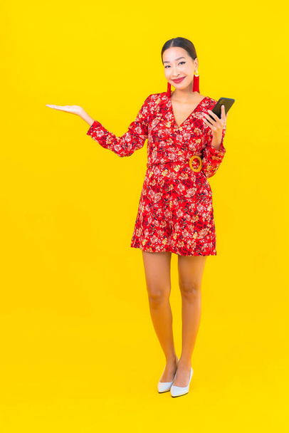 Portret piękny młody Azji kobieta używać inteligentny telefon komórkowy na żółtym tle kolor - Zdjęcie, obraz