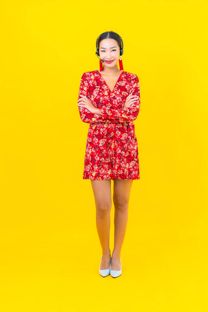 Muotokuva kaunis nuori aasialainen nainen, jolla on kuulokkeet asiakaspalvelukeskukseen keltaisella taustalla - Valokuva, kuva