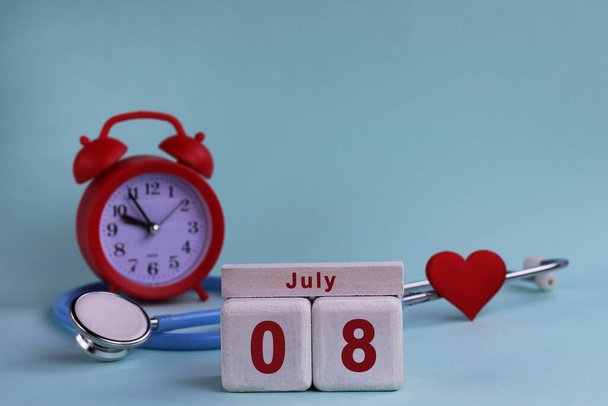 8 июля. Белый деревянный календарь блоков с датой, часами и стетоскопом на голубом пастельном фоне. Выборочный фокус. концепция здоровья. - Фото, изображение