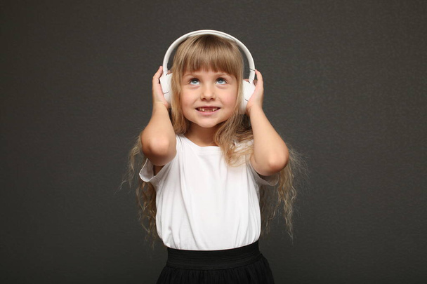 child girl enjoys music in her big white headphones and smile.Blue eyes blonde hair girl standing and listen to music. High quality photo - Photo, Image