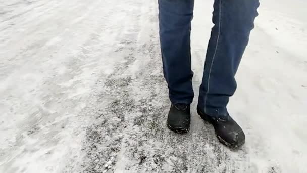 Henkilön jalat talvisaappaissa ja farkuissa kävelevät lumen peittämällä asfaltilla. Talvi vaellus käsite. Matala näkymä, hidastus 240 fps. - Materiaali, video