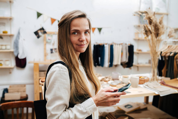 Portrait of a young woman standing in an ecological shop with a phone in hand - Фото, изображение