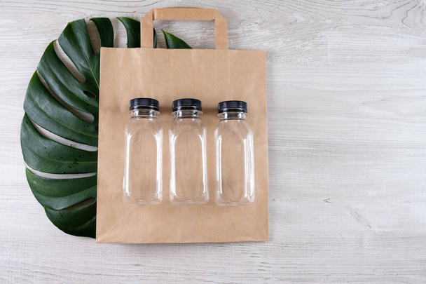 Three plastic bottles on a brown paper eco bag. Place for your logo. Eco-friendly food packaging and cotton eco bags on gray background with copy space. containers for catering and street fast food. - Photo, Image