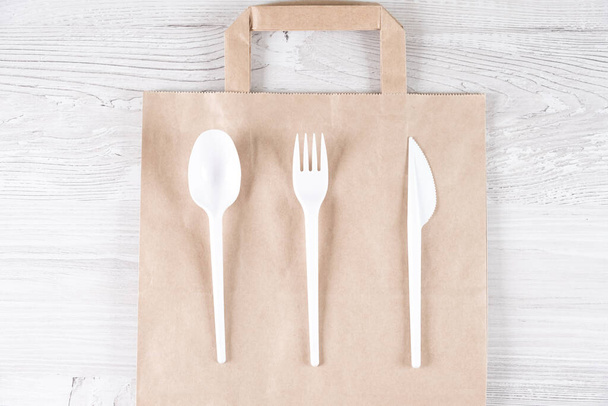 plastic fork, spoon, knife on paper bag. Eco-friendly food packaging and cotton eco bags on gray background with copy space. Carering of nature and recycling concept. containers for catering and - Fotografie, Obrázek