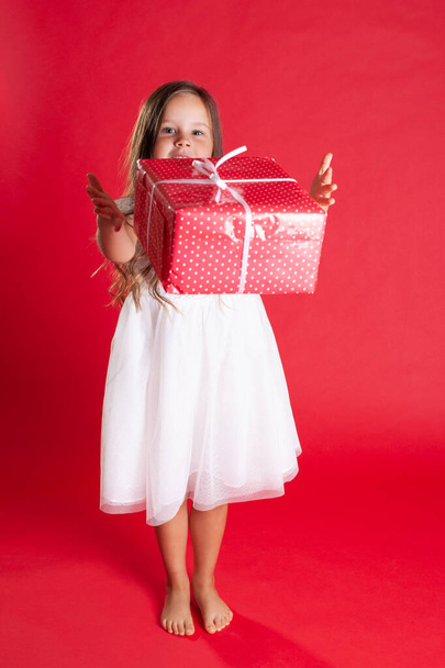full-length beautiful girl in a white dress and barefoot throws a gift box in the air, isolated on a vibrance background - Foto, Imagen