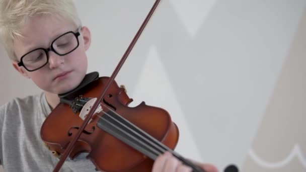 Ένα όμορφο ξανθό αγόρι με γυαλιά μαθαίνει να παίζει βιολί.. - Πλάνα, βίντεο