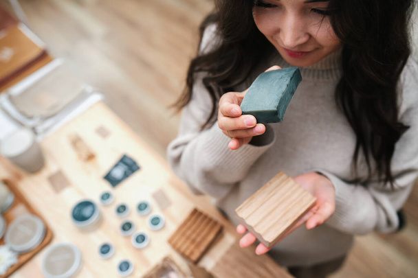 Blissful woman holds eco soap and wooden soap dish. Smelling soap. Overhead view - Foto, Imagem