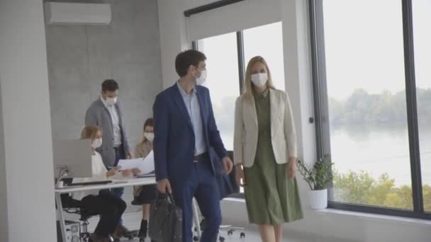 Jóképű fiatal üzleti pár együtt sétálnak, miközben védőmaszkot viselnek, hogy megakadályozzák a koronavírust az irodahelyiségben. - Felvétel, videó