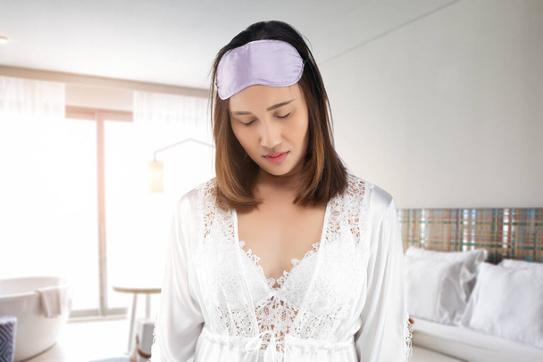 Kobieta w białej satynowej koszuli nocnej, ubrana w koronkowy szlafrok, śpiąca rano w sypialni. Lenistwo kobieta śpi stojąc rano - Zdjęcie, obraz